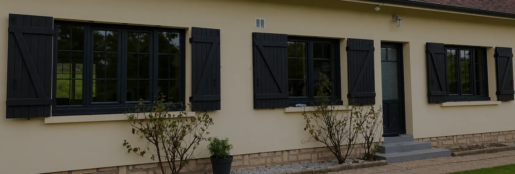 Fenêtres aluminium noir sur façade claire avec volets battants et plantes devant